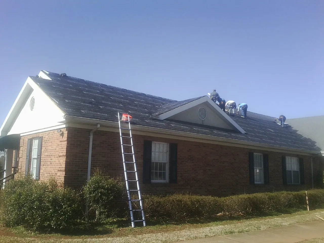 Crew tearing shingles off a brick ranch roof with a ladder set — Emergency Roof Repair work by our crew in Arion