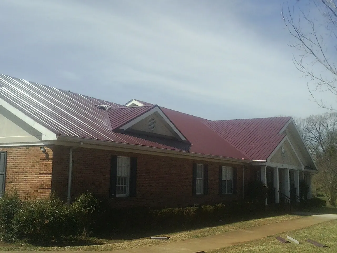 Red metal roof with gabled entries on a long brick building, from a Hail Damage Roof Repair job in Arion