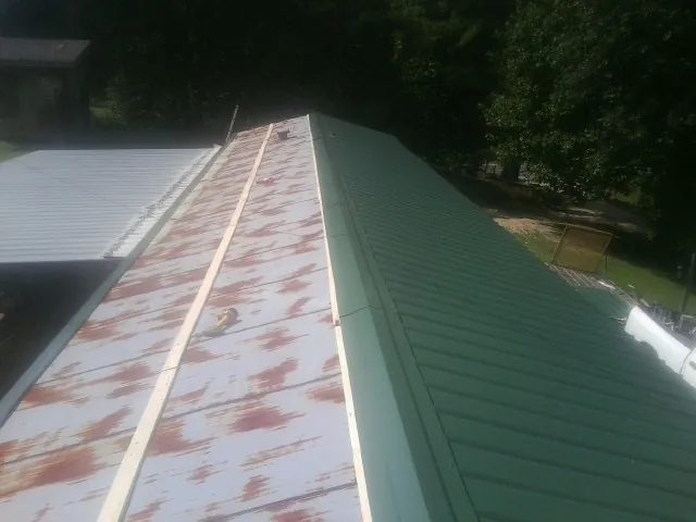Old rusted panels beside newly installed green metal roofing — Wind Damage Roof Repair by Roofing Brothers in Arion