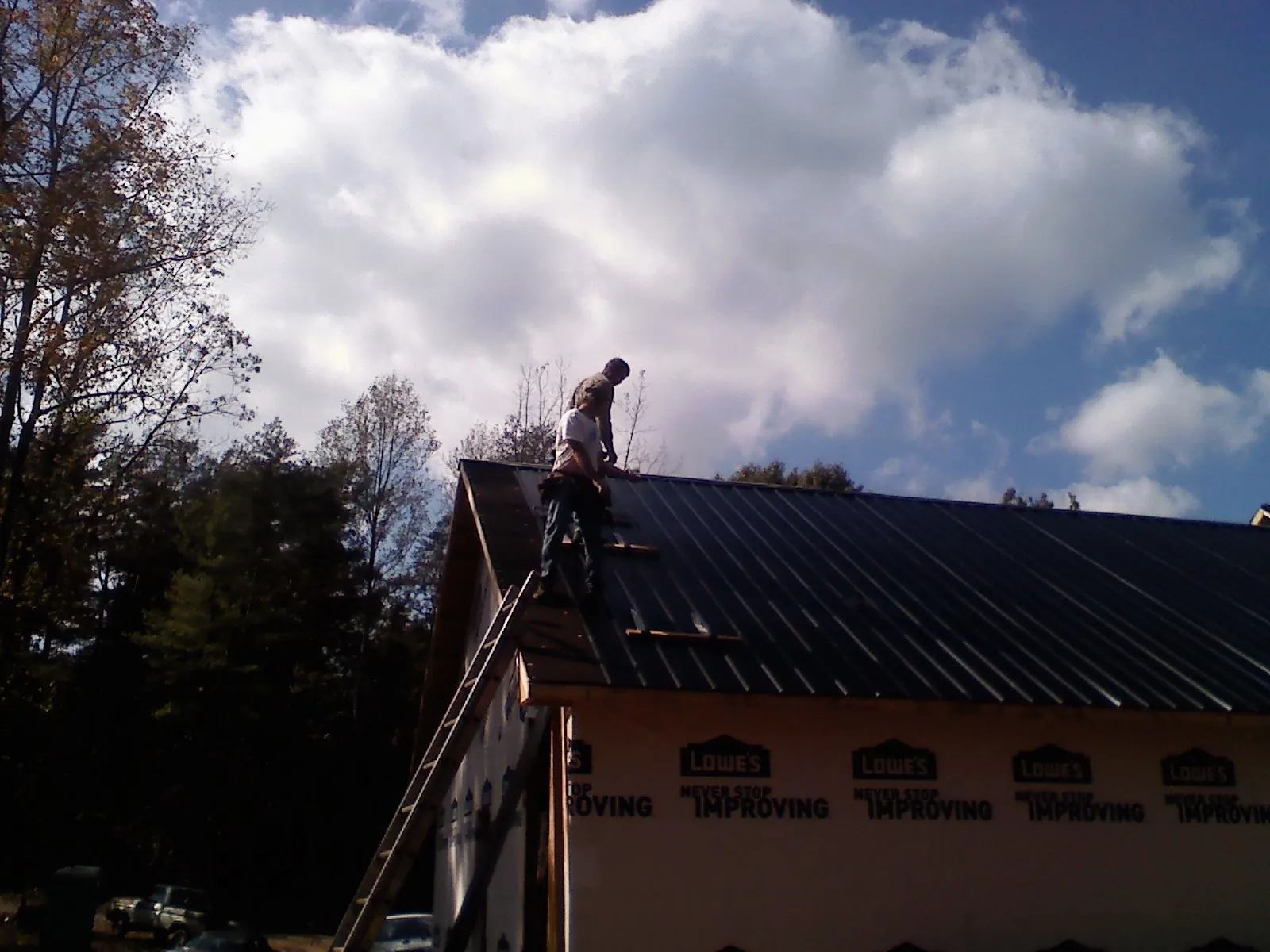 Roofer fastening dark metal panels high against a cloudy sky, from a Roof Inspection job in Arion
