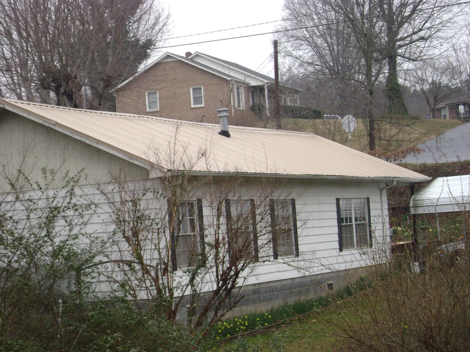 Tan metal roof on a white sided house set into a hillside — Commercial Roofing by Roofing Brothers in Arion